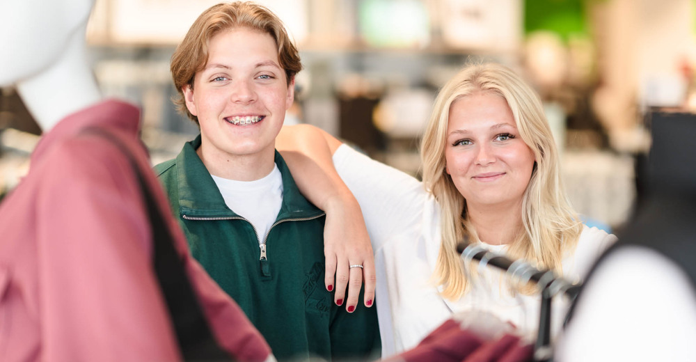 Två glada elever bland provdockor och klädställningar i en butik.
