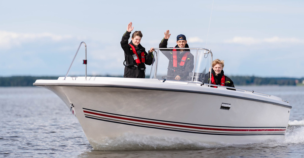 Tre glada elever vinkar från en motorbåt ute på sjön.