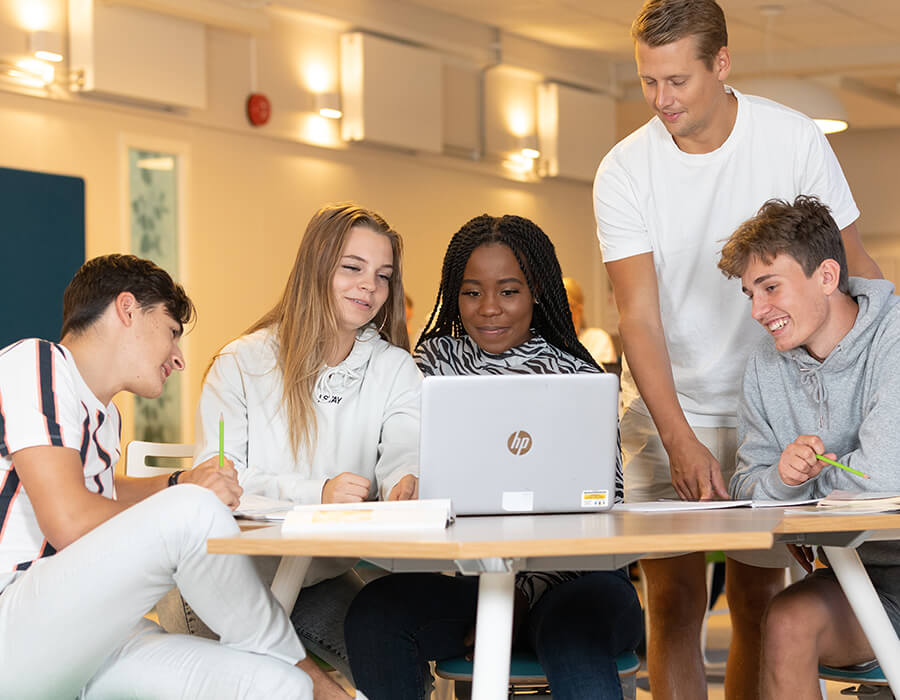 Grupp av elever sitter runt ett bord och tittar på en dator. 